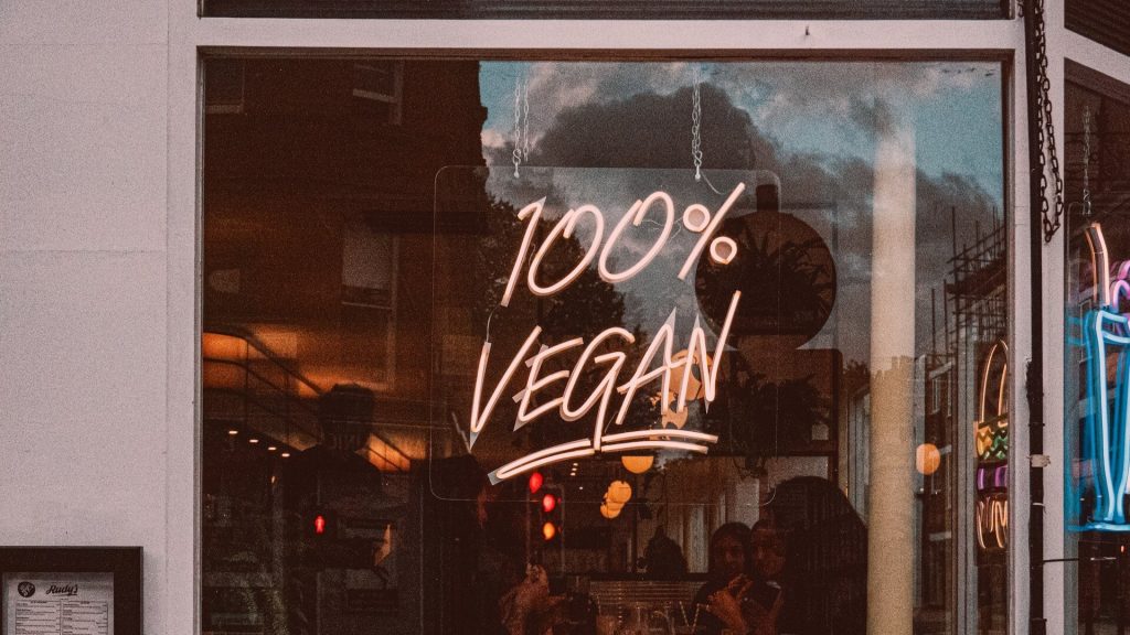 A bright neon sign inside a restaurant that proudly declares "100% Vegan" in vibrant colors.